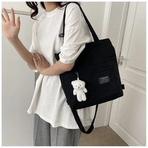 Detail of black canvas tote bag with fashion tag and cute white bear keychain accessory