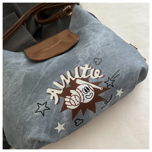 Dettaglio della borsa a tracolla in denim blu con stampa cartoon e patta in pelle marrone