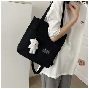 Detail shot of a black canvas tote with a white teddy bear charm and side pocket