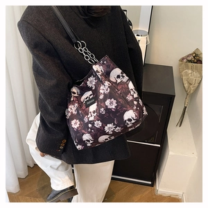 Close-up of a black crossbody bag with skull and flower prints and metal chain strap