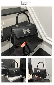 Detail of black bow square bag showing glossy leather and silver metal bow buckle