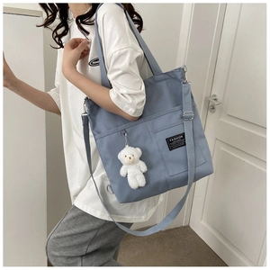 Detail of blue canvas tote bag featuring front pocket and cute white teddy bear charm