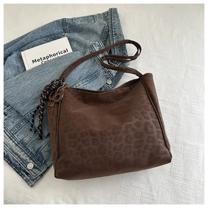 Detail of dark brown leopard print tote bag with woven pendant on white background