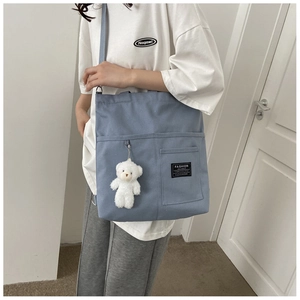 Detail of blue canvas tote bag featuring front pocket and cute teddy bear charm