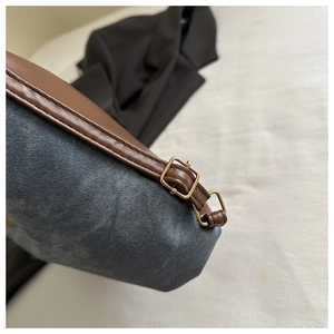 Dettaglio del tessuto denim blu con finiture in pelle marrone e fibbie dorate sulla borsa