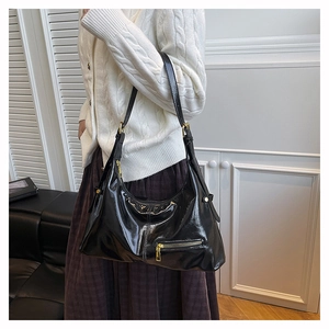 Detail of black patent leather hobo bag with glossy finish and gold hardware on a model