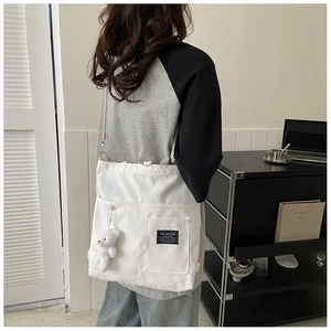 Detail of white canvas crossbody bag with front pockets and cute plush bear charm