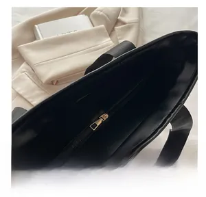 Detail of smooth gold zipper closure on minimalist black tote bag with woven strap