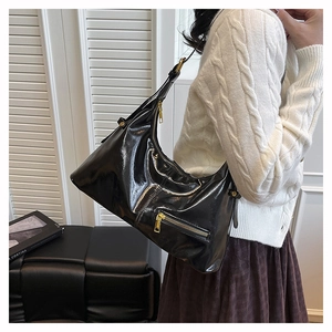 Detail of glossy black patent leather hobo bag with gold hardware worn over the shoulder