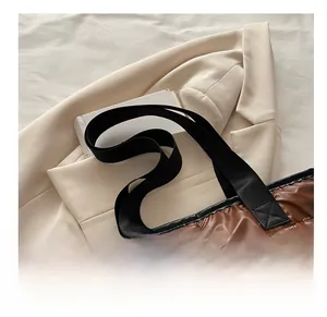 Detail of a brown quilted down tote bag with black woven handles on a beige blazer
