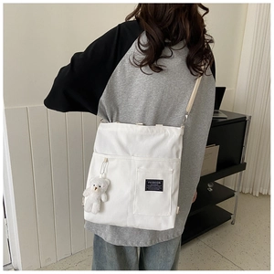 Back view of a white canvas crossbody bag with adjustable strap and bear pendant