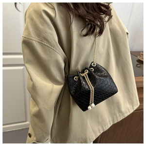 Dettaglio di una borsa a secchiello nera intrecciata con catena dorata e perle bianche