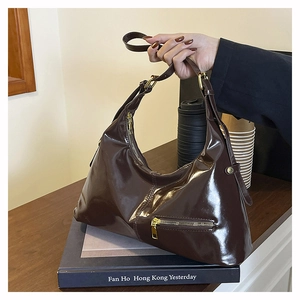 Detail of glossy brown hobo shoulder bag with golden zipper on a vintage wooden desk