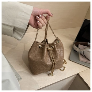 Dettaglio borsa a secchiello marrone intrecciata con catena dorata e perla decorativa