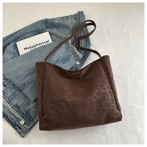 Detail of a large brown leopard print tote bag placed on white bedding with a denim jacket