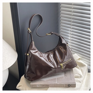 Detail of a dark coffee glossy patent leather hobo bag with gold metal hardware and zippers