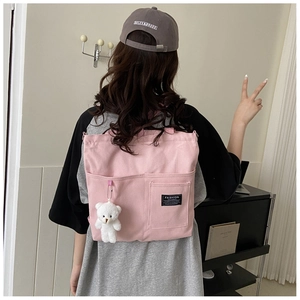 Detailed back view of pink canvas tote bag with side pockets and plush bear charm decoration