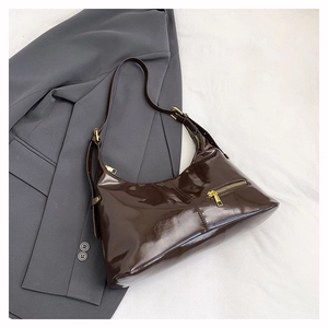 Detail of glossy dark brown leather shoulder bag with golden zipper on a grey blazer