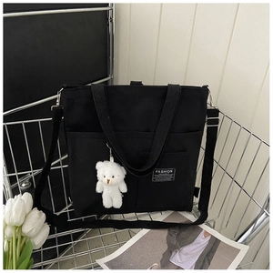 Detail of black canvas tote bag with front pocket and cute white plush bear pendant decor