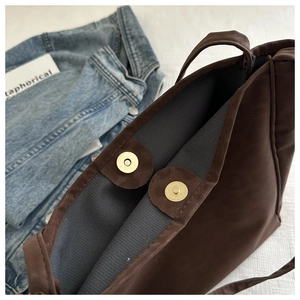 Detail of magnetic buckle closure on a dark brown matte tote bag with striped lining
