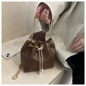 Dettaglio borsa a secchiello intrecciata marrone con catena dorata e perle sul cordoncino