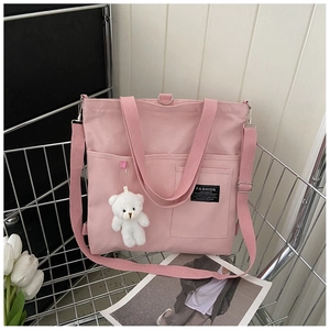 Pink canvas tote bag featuring a teddy bear charm and adjustable strap in a wire basket