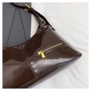 Detailed macro view of dark brown glossy patent leather texture with gold zipper pocket