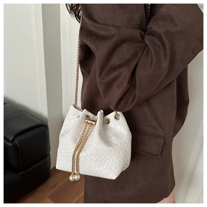Dettaglio borsa a secchiello bianca intrecciata con catena d'oro e nappe di perle