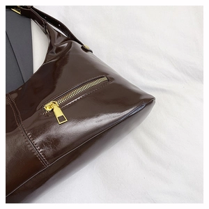 Detailed view of dark brown patent leather tote with shiny finish and gold zipper detail