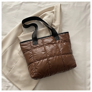 Détail d'un sac cabas matelassé marron avec de larges anses noires sur un lit