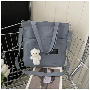 Detail of blue-grey canvas tote bag with adjustable strap and bear pendant in shopping cart