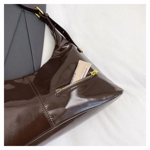 Detail of dark brown patent leather tote showing golden zipper pocket and glossy texture