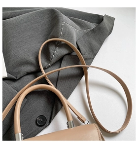 Detailed close-up of beige leather bag handle with silver metal rings and shoulder strap