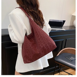 Detailed view of large burgundy leopard embossed tote bag on a model's shoulder