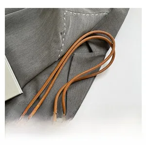 Detail of brown leather bag featuring tied cylindrical straps and high-quality stitching