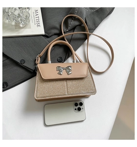 Detail view of bow handbag showing beige leather and gold glitter stitching textures