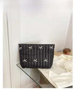 Detail of black quilted pouch with white bow embroidery and smooth glossy finish
