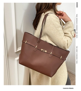 Side view of a brown leather tote bag with gold metal buckle on light cream coat