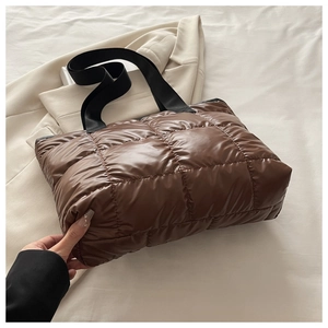 Détail d'un sac cabas matelassé marron avec de larges anses noires sur du linge