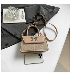 Detail of beige sequin bow handbag showing textured PU leather and silver metal bow
