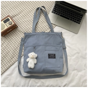 Flat lay of blue canvas tote bag with bear charm and adjustable shoulder strap