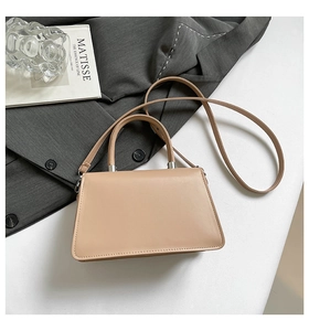 Minimalist beige bow handbag with silver hardware and adjustable strap on a gray blazer
