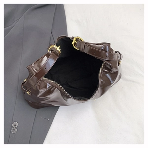 Detail view of glossy dark brown dumpling bag with gold buckle on gray blazer background