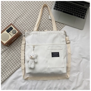 Detail view of canvas tote bag with shoulder strap and plush bear charm on white desk