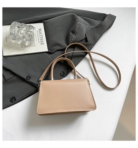 Detail of khaki leather handbag with round handle next to art book and blazer