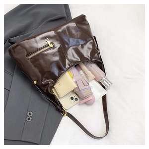 Detail of dark brown oil wax leather tote bag with gold zipper on grey blazer background