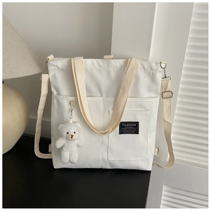 Detail of white canvas tote bag with adjustable strap, plush bear charm and fashion label