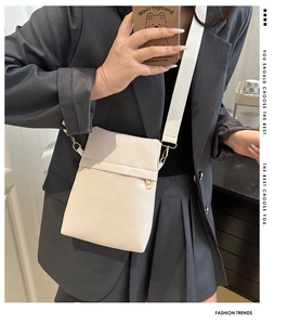 Close-up of white pebble leather crossbody bag with wide strap and gold hardware