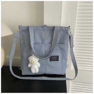 Close-up of light blue canvas tote bag showing the branded label and plush bear charm