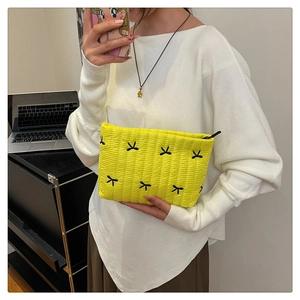 Detail of yellow quilted clutch with black bow embroidery and textured wavy fabric